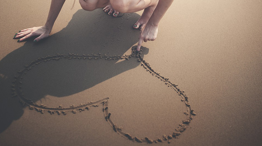 Mão desenhando um coração na areia.