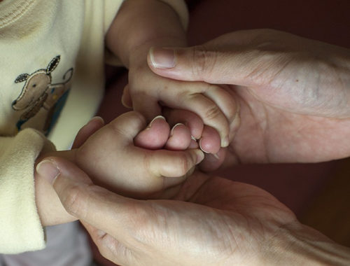 Mãos mais velhas segurando mãos de uma criança pequena.