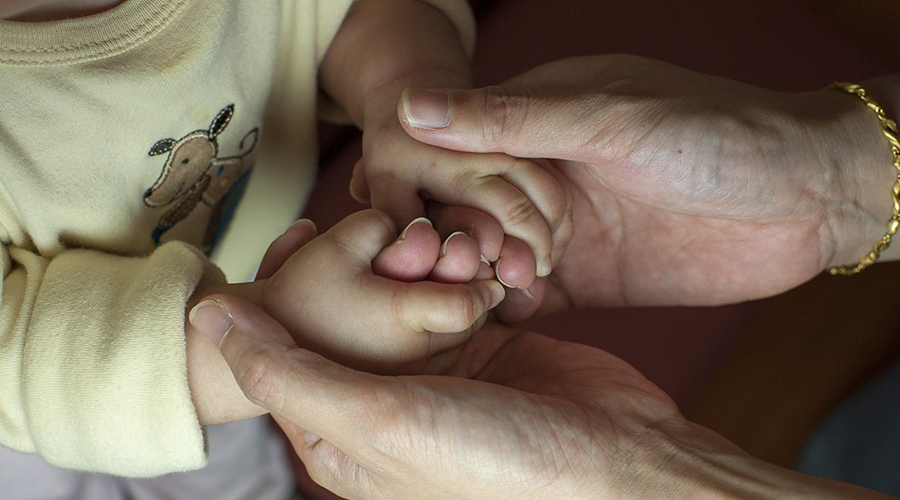 Mãos mais velhas segurando mãos de uma criança pequena.