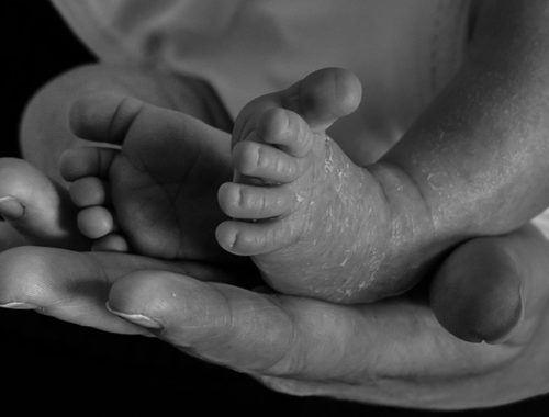 Imagem em preto e branco de pés de um bebê sob mãos adultas.