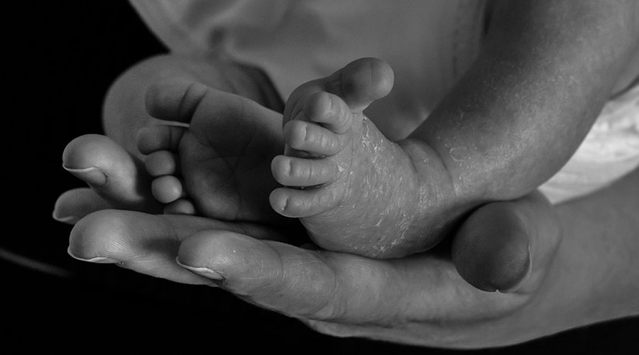Imagem em preto e branco de pés de um bebê sob mãos adultas.