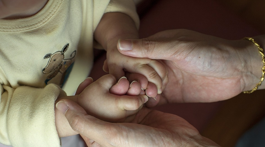 Mãos de uma criança sendo seguradas pelas mãos de uma pessoa mais velha.