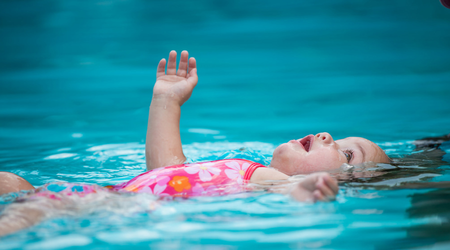Criança com maiô rosa boiando em uma piscina.