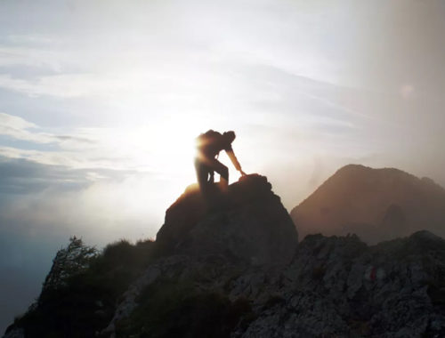 Pessoa chegando ao topo de uma montanha com o sol ao fundo.