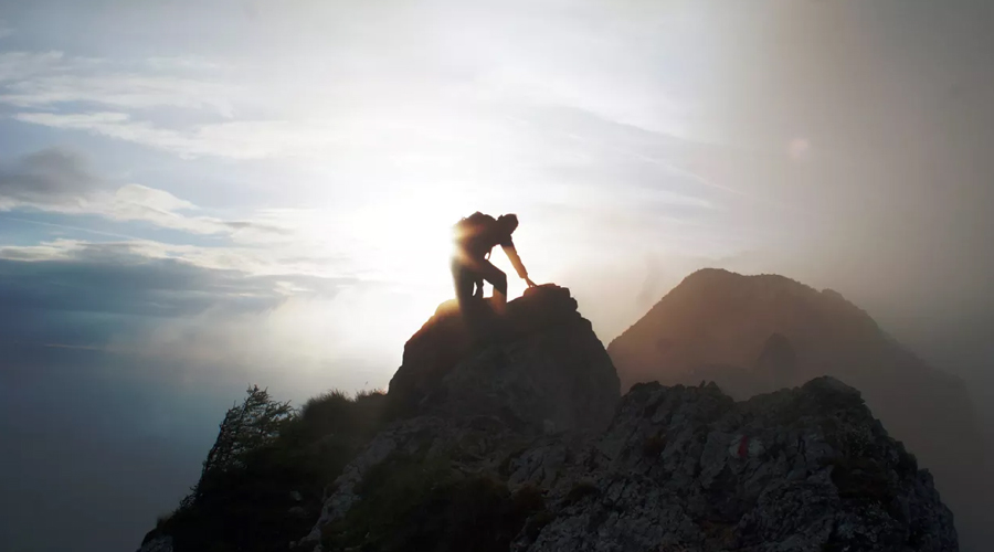 Pessoa chegando ao topo de uma montanha com o sol ao fundo.