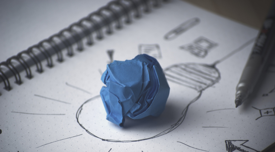 Papel azul amassado feito bolinha em cima de um papel branco com um desenho de uma lâmpada.