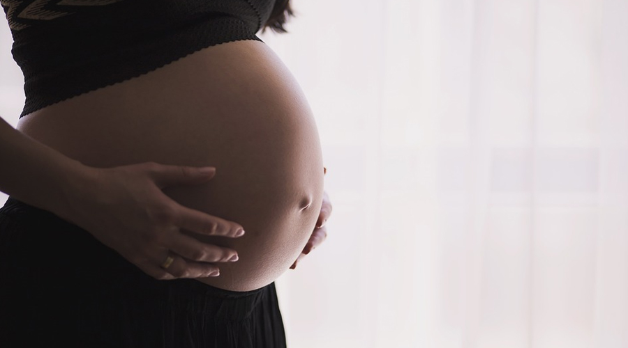 Imagem mostra barriga de uma mulher grávida de lado e as mães da mulher tocando a barriga.