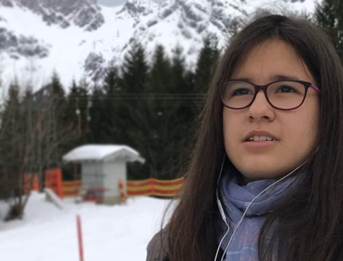 Foto do rosto de uma menina de frente com montanhas de neve ao fundo.